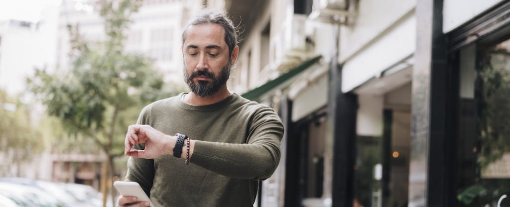 Man holding smart phone checking time on wristwatch