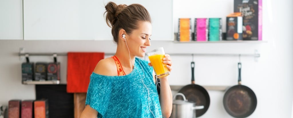 Une femme boit du jus dans sa cuisine