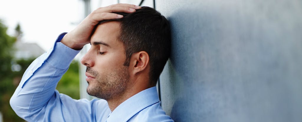 Un homme pose sa tête contre un mur. Il est stressé parce que ses comptes sont en cours de recouvrement.