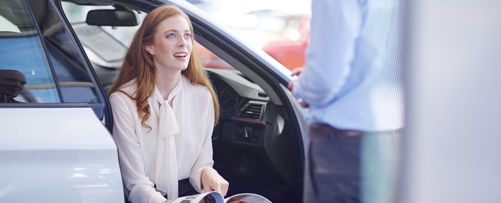 Car dealer talks to client as she reviews options at the dealership