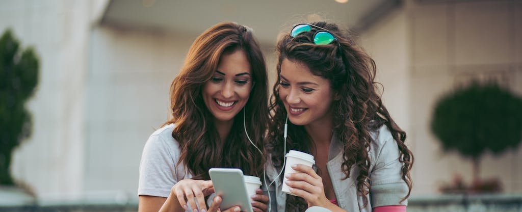 Two women sitting on staircase and listening to music on mobile phone