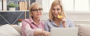 Adult woman and daughter shopping online with credit card and laptop.