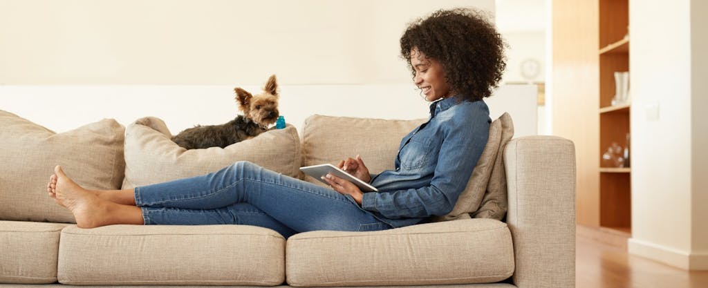 Young woman relaxing on sofa with her dog and looking at her digital tablet