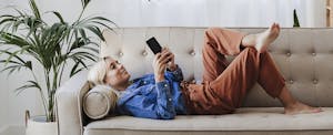 Young woman using mobile phone lying on sofa at home