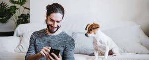 Man with laptop using mobile phone while sitting by dog at home
