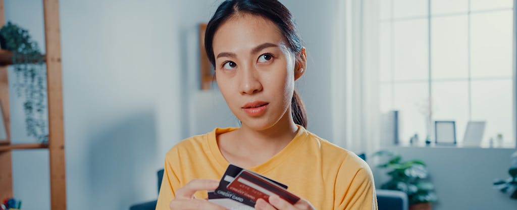 Young Asian woman holding credit card making payment online at desk in living room at home.