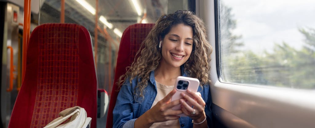 Happy woman commuting on a train and checking her cell phone