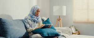 Close up young Asian muslim woman with hijab using tablet calculator focus on utility bills calculate check credit card receipt monthly expense bill on sofa at house.