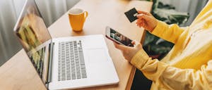 Shot of laptop with person's hands holding a phone and credit card