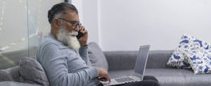 Latino man is inside the office where he works with his laptop in his hands with which he does his pending work while standing at the door of his office