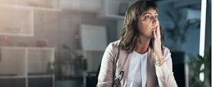 Woman at desk staring pensively into middle distance